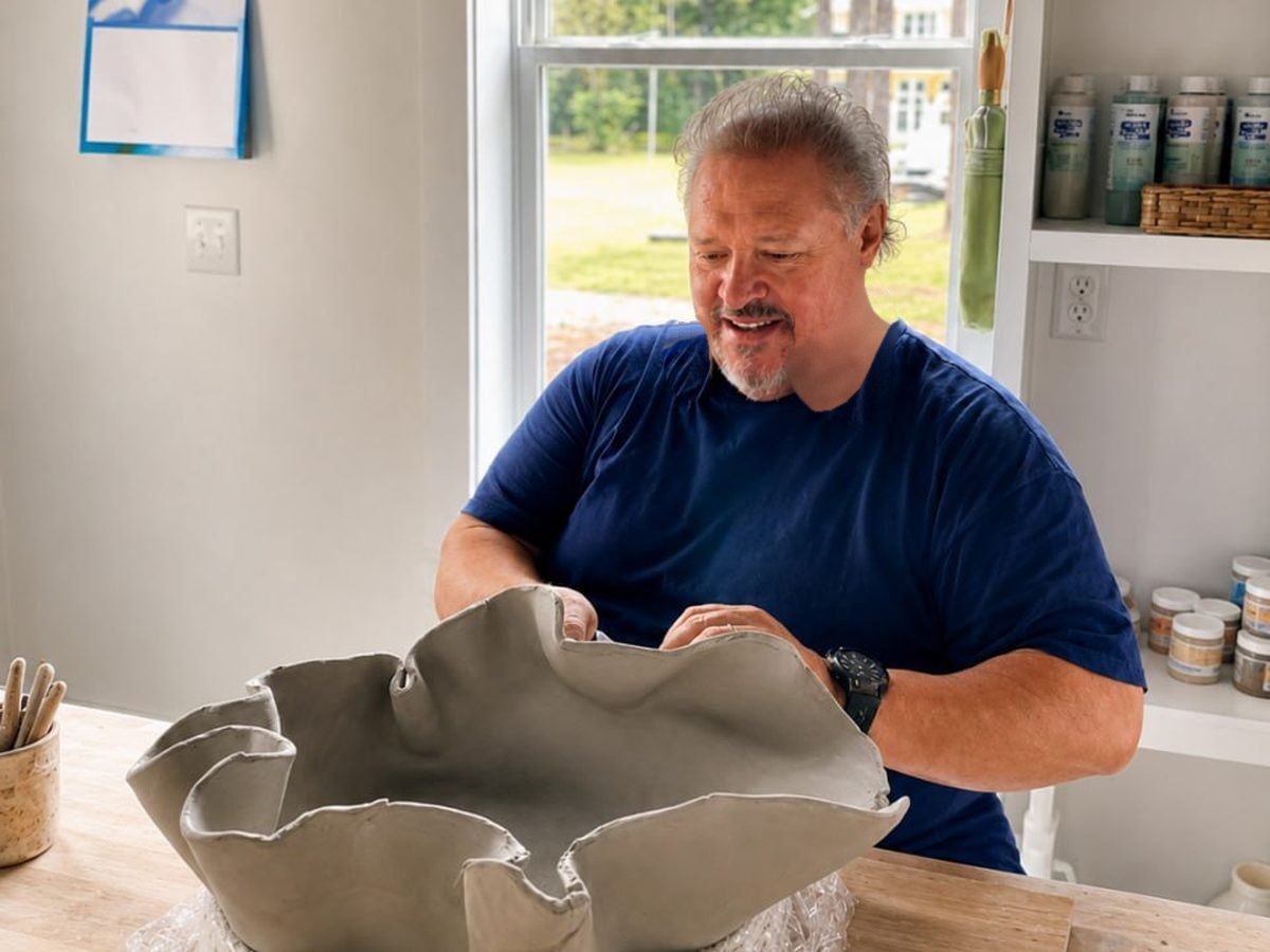 A potter smiling at the wide ruffled clay bowl he has just built by hand